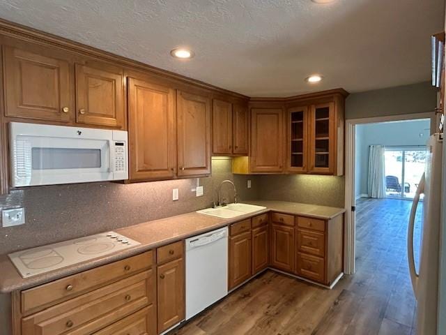 kitchen with a sink, glass insert cabinets, wood finished floors, white appliances, and light countertops