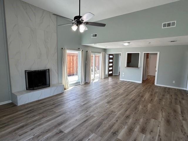 unfurnished living room featuring visible vents, a ceiling fan, a tiled fireplace, wood finished floors, and baseboards