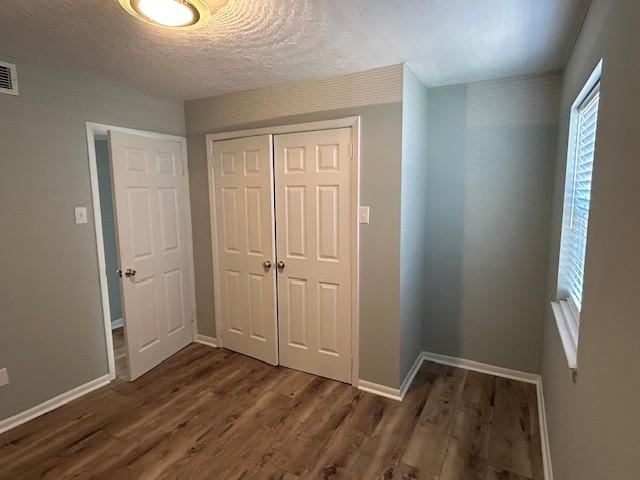 unfurnished bedroom featuring a closet, baseboards, a textured ceiling, and dark wood finished floors