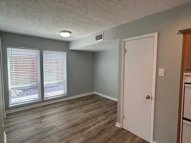 spare room featuring baseboards, wood finished floors, visible vents, and a textured ceiling