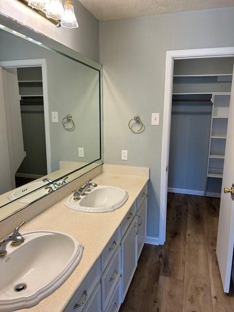 full bathroom with a sink, a walk in closet, a textured ceiling, and wood finished floors