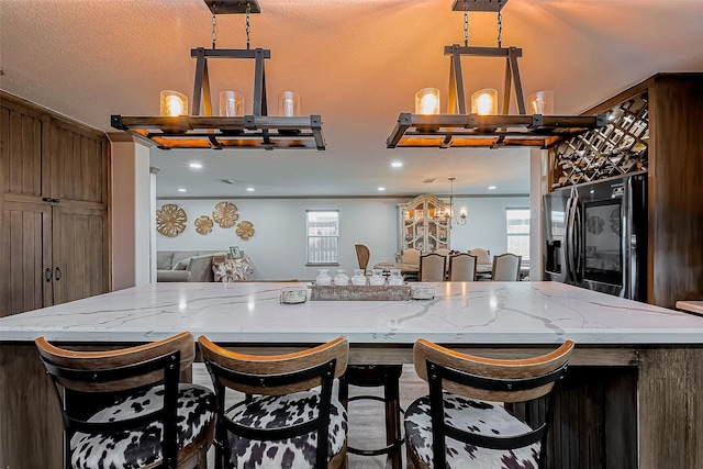 kitchen featuring a wealth of natural light, refrigerator with ice dispenser, pendant lighting, and light stone countertops