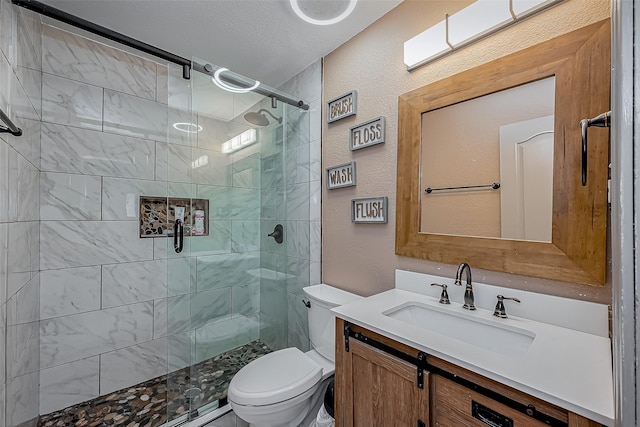 full bath with toilet, a stall shower, a textured wall, a textured ceiling, and vanity