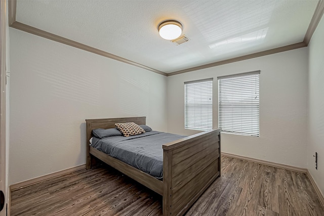 bedroom featuring visible vents, baseboards, wood finished floors, and crown molding