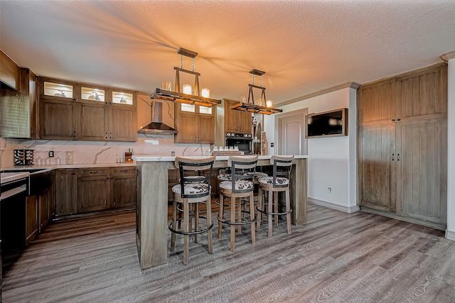 kitchen with a center island, light countertops, wall chimney range hood, and wood finished floors