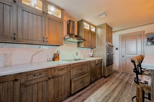 kitchen with wood finished floors, visible vents, wall chimney range hood, black electric cooktop, and tasteful backsplash