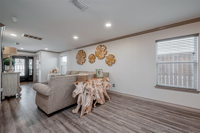 living area with visible vents, baseboards, dark wood-type flooring, and ornamental molding