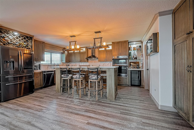 kitchen featuring a notable chandelier, beverage cooler, stainless steel appliances, wall chimney range hood, and light countertops