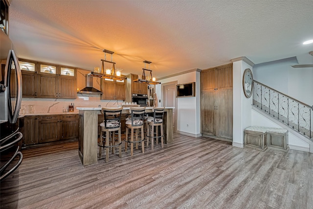 kitchen with wood finished floors, a kitchen island, wall chimney exhaust hood, and freestanding refrigerator