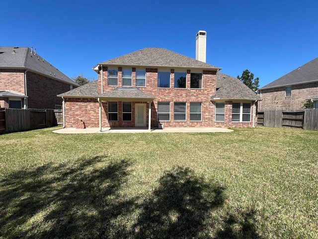 rear view of property with brick siding, a lawn, a chimney, and a fenced backyard