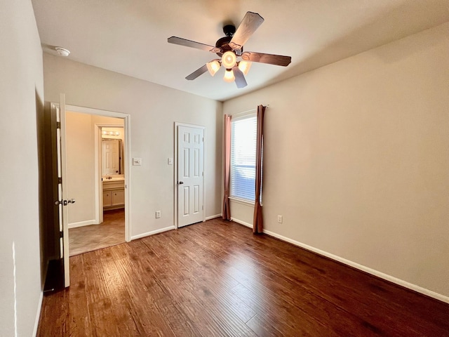 unfurnished bedroom with dark wood-type flooring, connected bathroom, baseboards, and ceiling fan