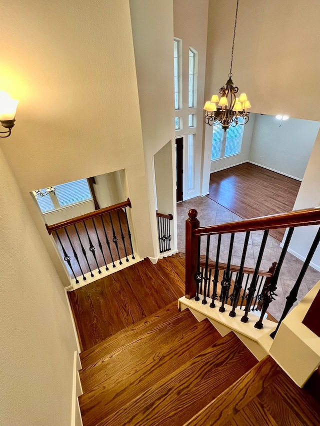 staircase featuring baseboards, wood finished floors, an inviting chandelier, and a towering ceiling