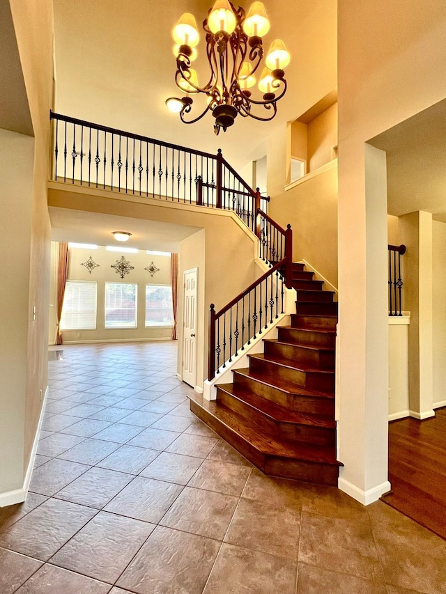 staircase with tile patterned flooring, baseboards, a high ceiling, and an inviting chandelier