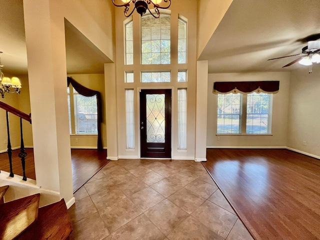 tiled foyer entrance featuring stairway, ceiling fan with notable chandelier, and baseboards