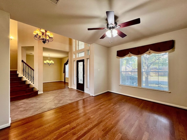 entryway with ceiling fan with notable chandelier, stairway, wood finished floors, and baseboards