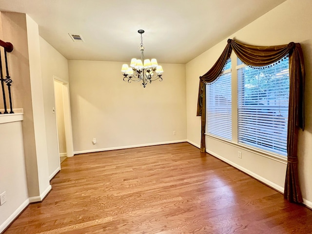 empty room featuring visible vents, baseboards, an inviting chandelier, and wood finished floors