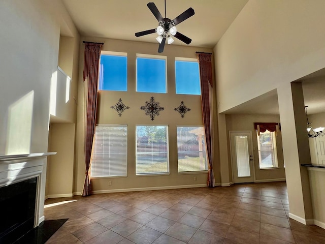 unfurnished living room featuring baseboards, a high ceiling, a fireplace, tile patterned floors, and ceiling fan with notable chandelier