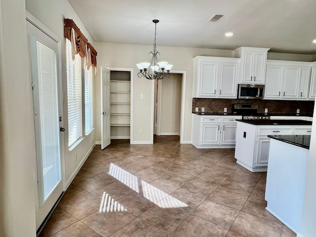 kitchen with dark countertops, white cabinetry, stainless steel appliances, an inviting chandelier, and light tile patterned flooring