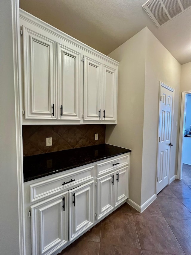 interior space featuring dark countertops, visible vents, decorative backsplash, white cabinets, and dark tile patterned flooring