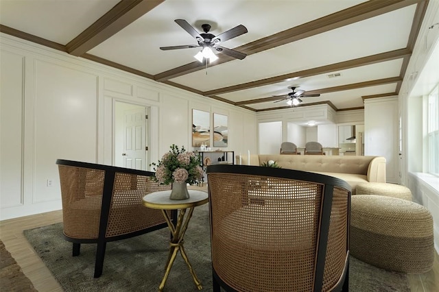 living area featuring beam ceiling, a decorative wall, crown molding, and ceiling fan