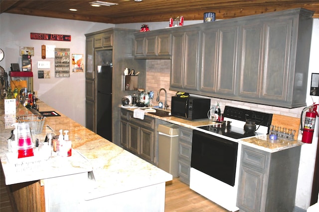 kitchen with black appliances, light wood finished floors, light stone countertops, and backsplash