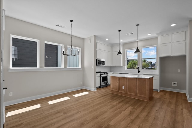 kitchen with light wood finished floors, light countertops, appliances with stainless steel finishes, a notable chandelier, and white cabinetry