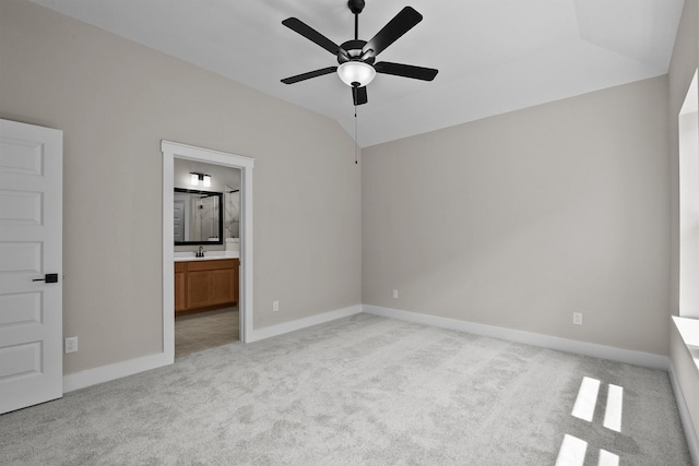 unfurnished bedroom featuring light carpet, lofted ceiling, a sink, ensuite bath, and baseboards