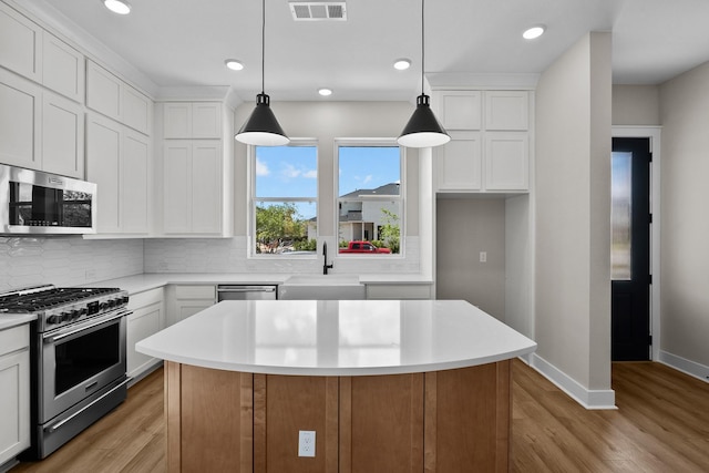 kitchen with light wood finished floors, a sink, decorative backsplash, light countertops, and appliances with stainless steel finishes