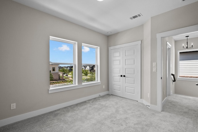 unfurnished bedroom featuring a notable chandelier, carpet, visible vents, and baseboards