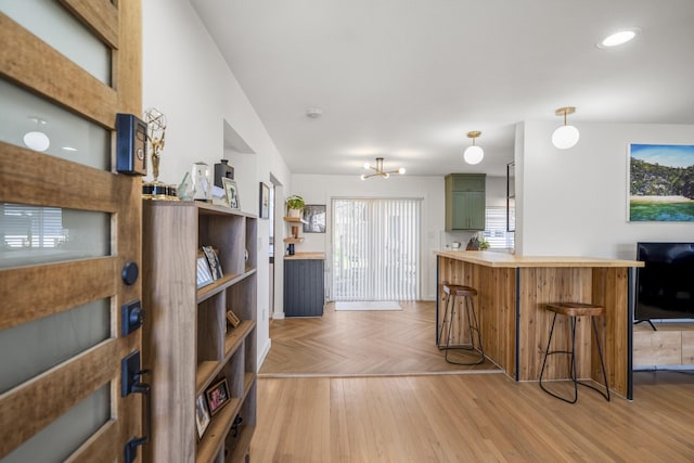 kitchen featuring a peninsula, light countertops, parquet flooring, green cabinets, and a kitchen breakfast bar