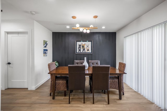 dining room with recessed lighting, wood walls, light wood finished floors, baseboards, and an accent wall