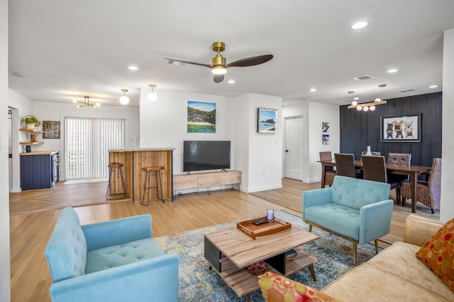 living room featuring visible vents, light wood finished floors, baseboards, recessed lighting, and ceiling fan with notable chandelier