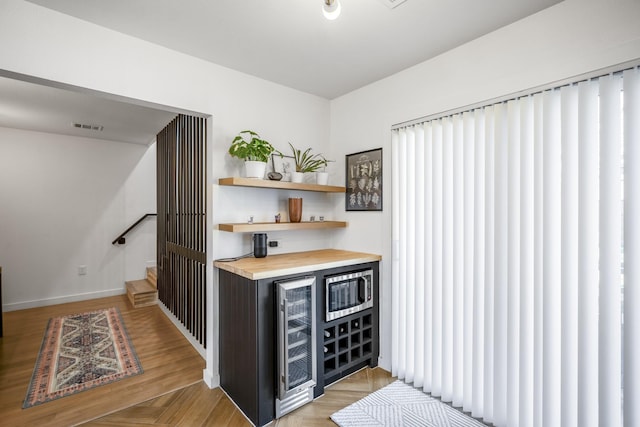 bar with visible vents, stainless steel microwave, beverage cooler, wood finished floors, and a bar