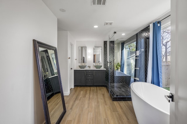 bathroom with visible vents, a stall shower, wood finished floors, a freestanding bath, and vanity