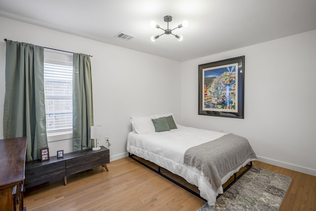 bedroom with visible vents, baseboards, an inviting chandelier, and wood finished floors