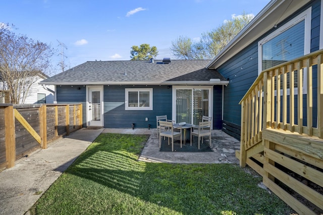 rear view of house with a patio, a shingled roof, a yard, and fence