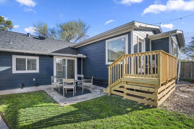 rear view of property with fence, a wooden deck, a shingled roof, a patio area, and a lawn