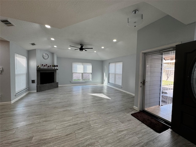 unfurnished living room featuring visible vents, a fireplace with raised hearth, lofted ceiling, and a ceiling fan