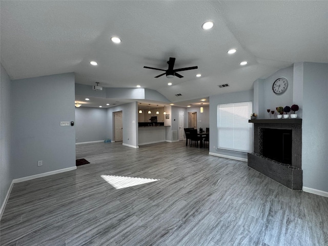 unfurnished living room with lofted ceiling, a fireplace with raised hearth, wood finished floors, baseboards, and ceiling fan