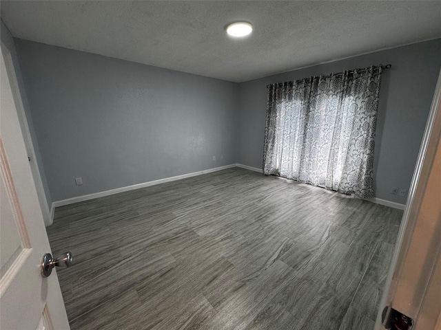 spare room with dark wood finished floors, a textured ceiling, and baseboards