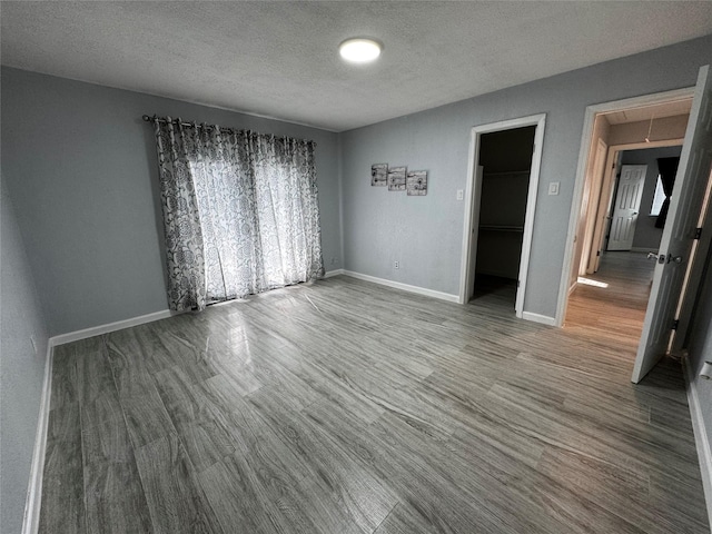 spare room with a textured ceiling, attic access, baseboards, and wood finished floors