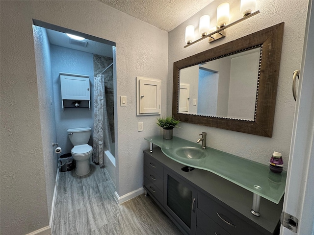 full bath featuring a textured ceiling, wood finished floors, toilet, and a textured wall