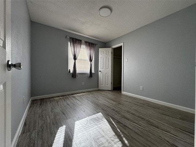 unfurnished bedroom featuring wood finished floors, baseboards, a textured wall, and a textured ceiling