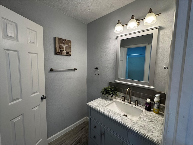 full bath with vanity, wood finished floors, baseboards, a textured ceiling, and a textured wall