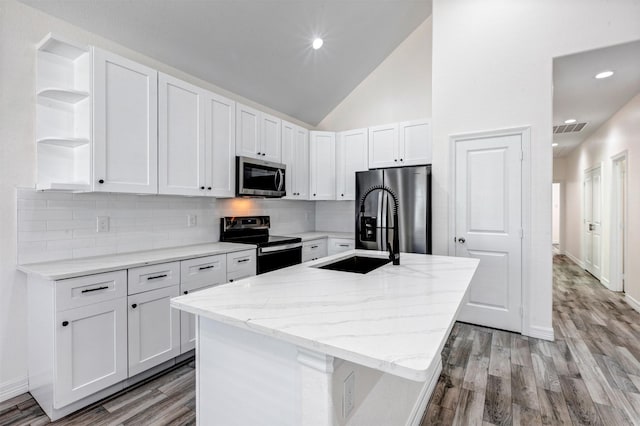 kitchen featuring an island with sink, a sink, open shelves, white cabinetry, and stainless steel appliances