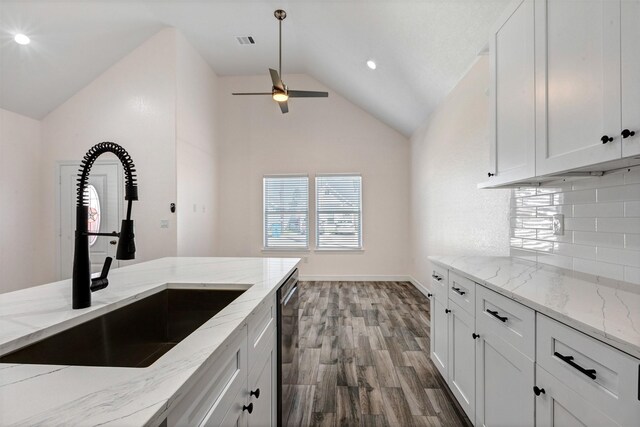 kitchen with vaulted ceiling, visible vents, white cabinetry, and a sink