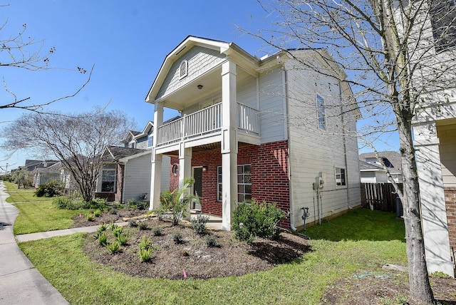 view of front of home with a front yard, a balcony, fence, and brick siding