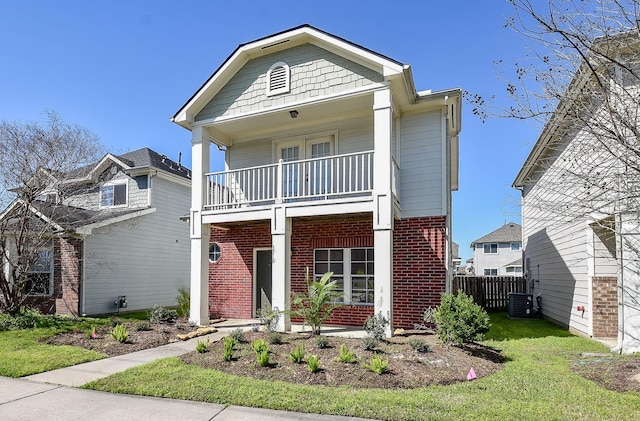 view of front of property featuring a balcony, fence, a porch, a front lawn, and brick siding