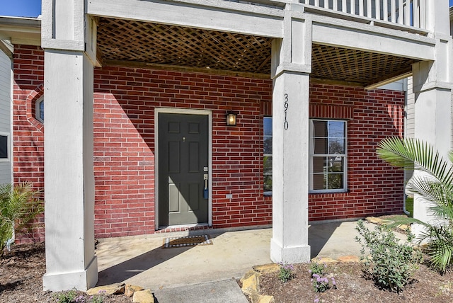 view of exterior entry featuring brick siding and a balcony