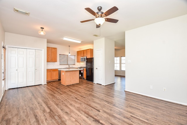 kitchen featuring wood finished floors, a ceiling fan, visible vents, a kitchen island, and appliances with stainless steel finishes